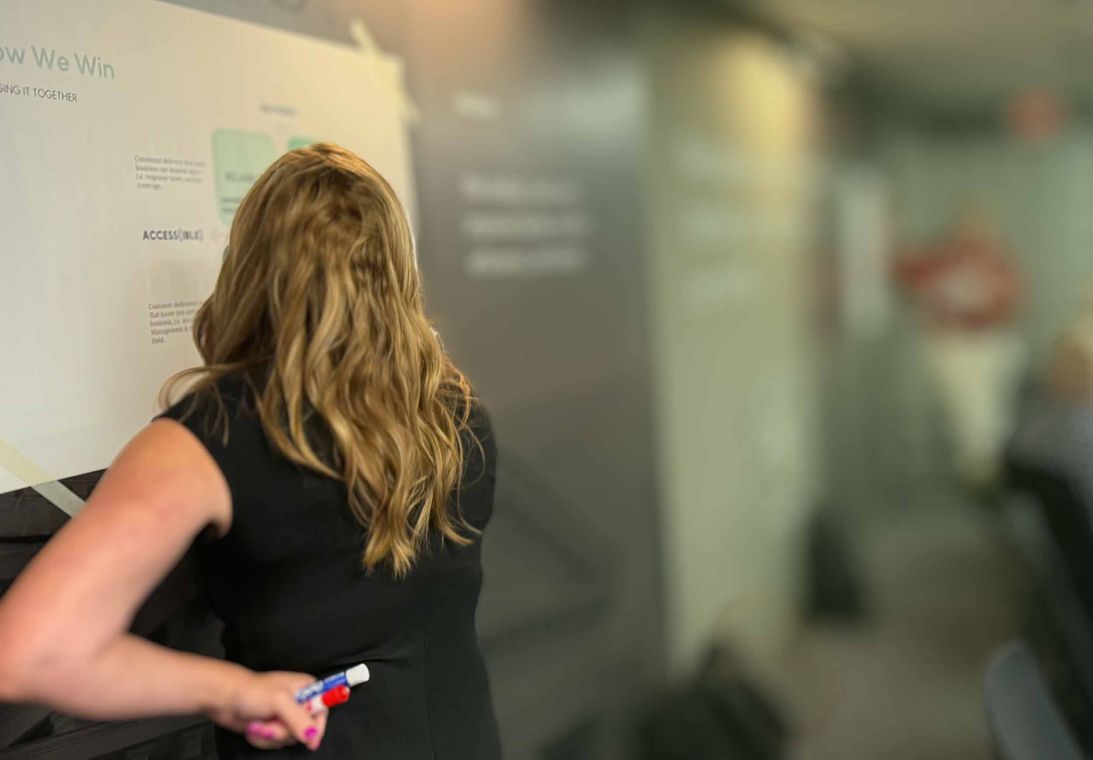 Facilitator leading a “How We Win” customer experience strategy workshop, writing on the board with a dry-erase marker