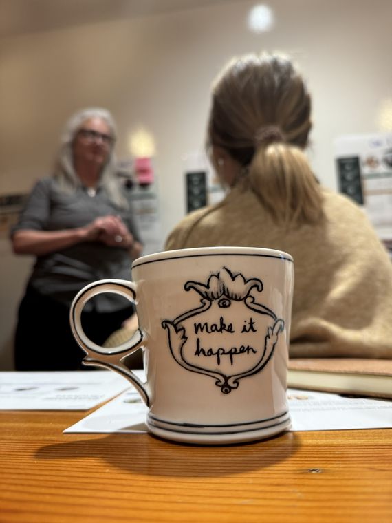 “Make it happen” mug on the table at a customer experience strategy workshop with participants in the background